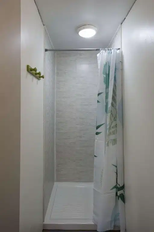 Salle de bain du gîte Le Repose Pieds avec une douche spacieuse et rideau de douche aux motifs tropicaux.